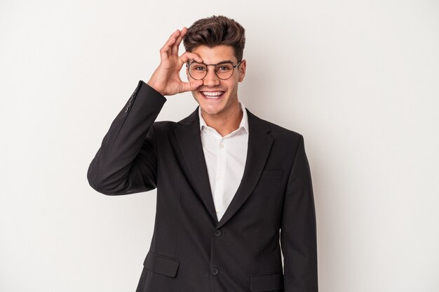 Young business caucasian man isolated on white background excited keeping ok gesture on eye.