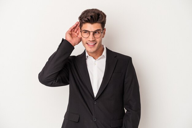 Young business caucasian man isolated on white background trying to listening a gossip.