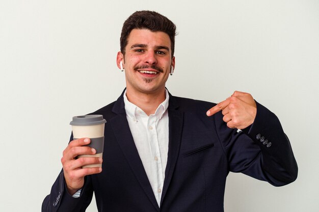 Young business caucasian man wearing wireless headphones and holding take way coffee isolated on white background person pointing by hand to a shirt copy space, proud and confident