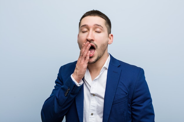 Young business caucasian man yawning showing a tired gesture covering mouth with him hand.