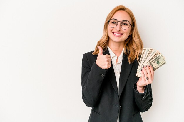 Young business caucasian woman holding banknotes isolated on white background smiling and raising thumb up