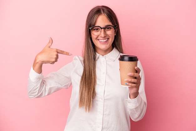 Young business caucasian woman holding a take away isolated on pink background person pointing by hand to a shirt copy space, proud and confident