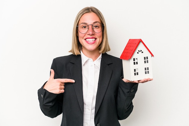 Young business caucasian woman holding a toy house isolated on white background person pointing by hand to a shirt copy space proud and confident