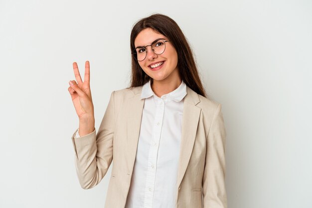 Young business caucasian woman isolated on white wall joyful and carefree showing a peace symbol with fingers