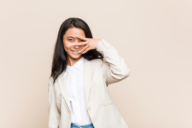 Young business chinese woman blink at through fingers, embarrassed covering face.