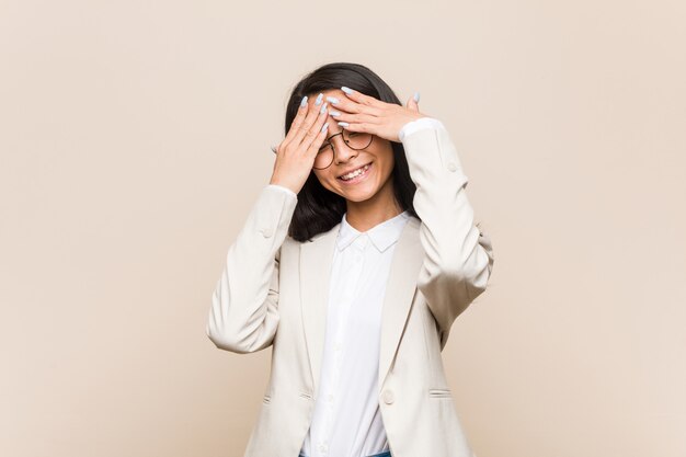 Young business chinese woman covers eyes with hands, smiles broadly waiting for a surprise.