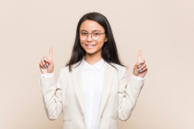 Young business chinese woman indicates with both fore fingers up showing a blank space.
