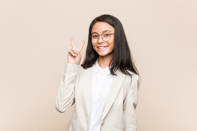 Young business chinese woman joyful and carefree showing a peace symbol with fingers.