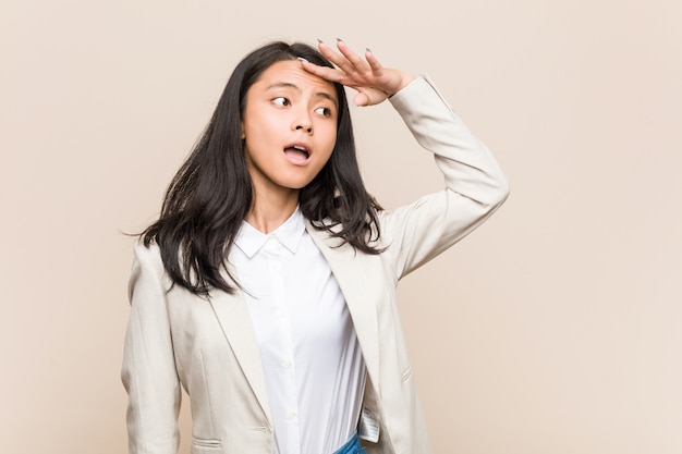 Young business chinese woman looking far away keeping hand on forehead.