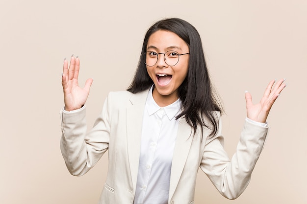 Young business chinese woman receiving a pleasant surprise, excited and raising hands.