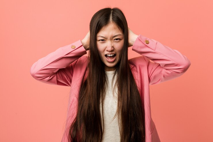 Photo あまりにも大きな音が聞こえないようにしようと手で耳を覆うピンクのスーツを着ている若いビジネス中国の女性。