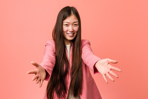 Young business chinese woman wearing pink suit feels confident giving a hug