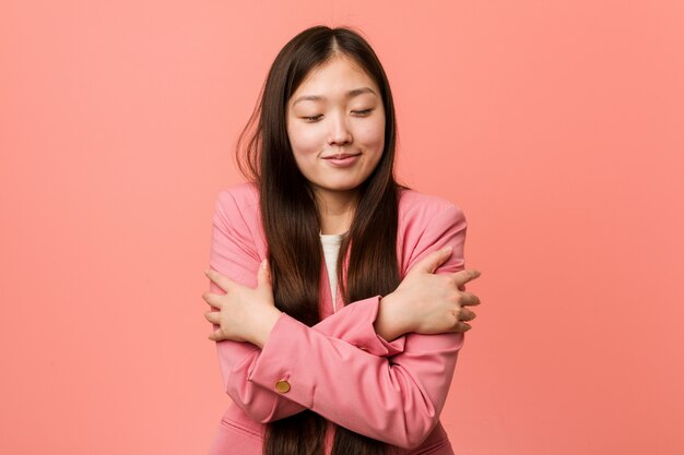 Photo young business chinese woman wearing pink suit hugs himself, smiling carefree and happy.