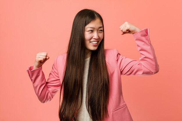 Young business chinese woman wearing pink suit raising fist after a victory, winner concept.