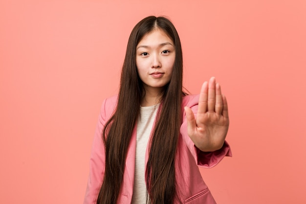 Young business chinese woman wearing pink suit standing with outstretched hand showing stop sign, preventing you.