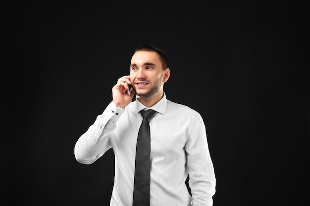 Young business coach speaking by cellphone on black background