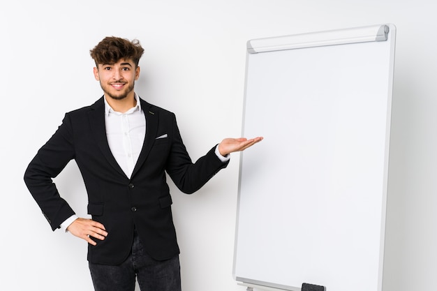 Young business coaching arabician man showing a copy space on a palm and holding another hand on waist.