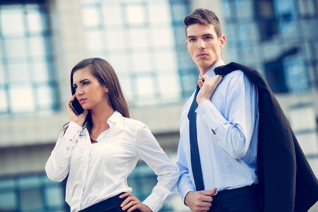 Фото Молодая деловая пара, стоящая перед офисными зданиями, и деловая женщина разговаривают по мобильному телефону.