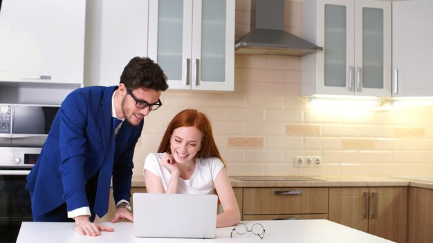 Young business couple talking and using laptop in kitchen at home.