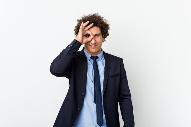 Young business curly man against white  excited keeping ok gesture on eye.