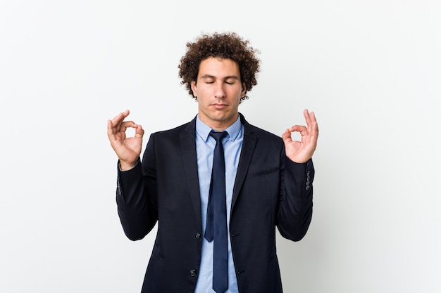 Young business curly man against white relaxes after hard working day, she is performing yoga.