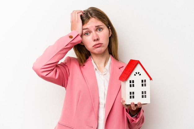 Young business English woman holding house toy isolated on white background being shocked she has remembered important meeting