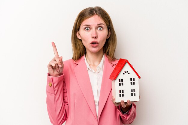 Young business English woman holding house toy isolated on white background having some great idea concept of creativity