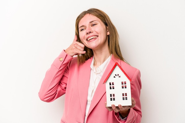 Young business English woman holding house toy isolated on white background showing a mobile phone call gesture with fingers.