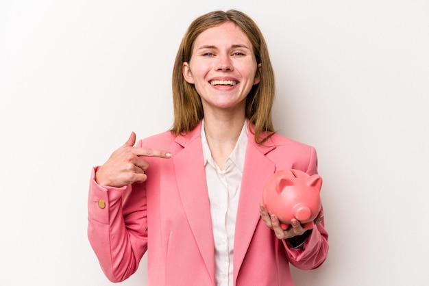 Young business English woman holding a piggybank isolated on white background person pointing by hand to a shirt copy space proud and confident