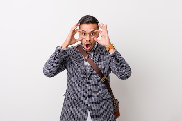 Young business filipino man against a white wall keeping eyes opened to find a success opportunity.