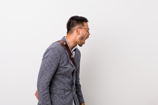 Young business filipino man against a white wall shouting towards a copy space