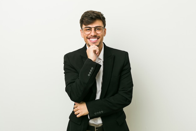 Young business hispanic man smiling happy and confident, touching chin with hand.