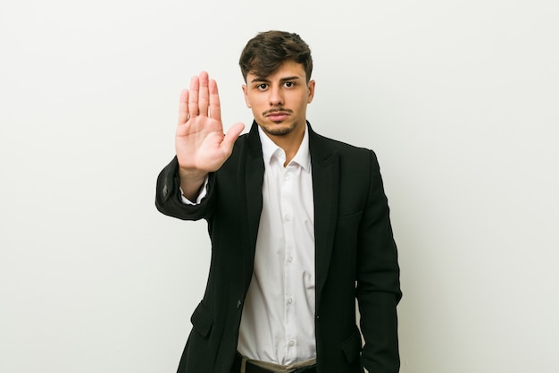 Photo young business hispanic man standing with outstretched hand showing stop sign, preventing you.