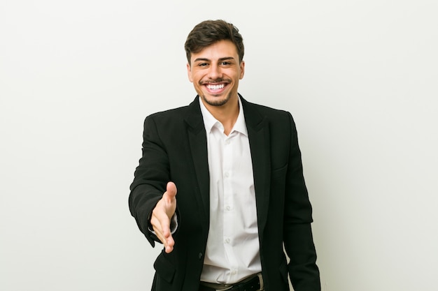 Young business hispanic man stretching hand at camera in greeting gesture.