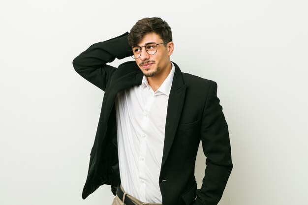 Young business hispanic man touching back of head, thinking and making a choice.