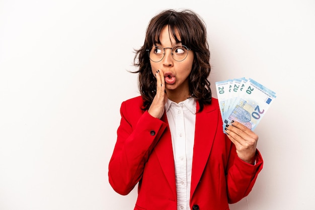 Young business hispanic woman holding banknotes isolated on white background is saying a secret hot braking news and looking aside