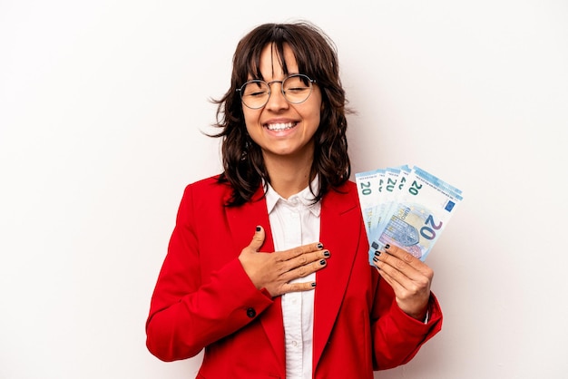 Young business hispanic woman holding banknotes isolated on white background laughs out loudly keeping hand on chest