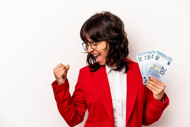 Young business hispanic woman holding banknotes isolated on white background raising fist after a victory winner concept