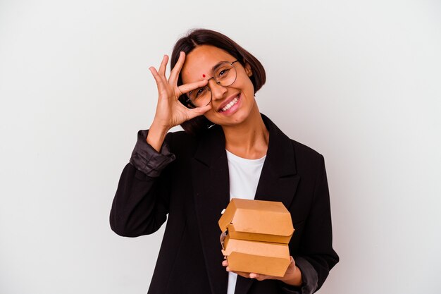 Young business indian woman eating burgers isolated excited keeping ok gesture on eye.