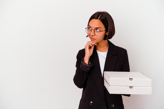 Young business indian woman holding pizzas isolated looking sideways with doubtful and skeptical expression.