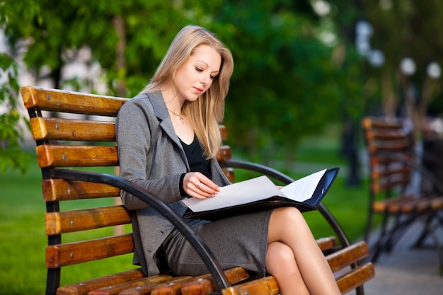 ベンチに座って、文書を読む若いビジネス女性