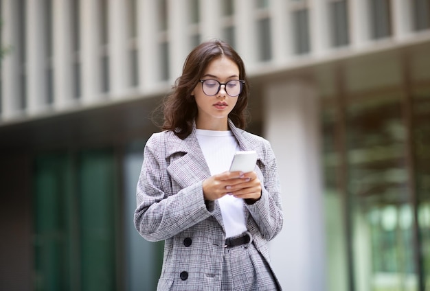 現代のビジネス センターの近くで携帯電話を使用している若いビジネス女性