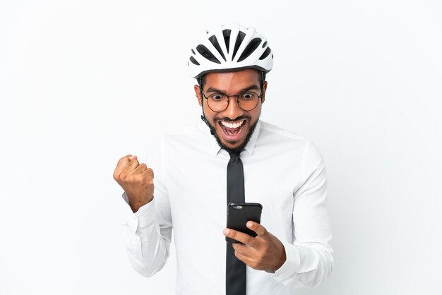 Young business latin man holding a bike helmet isolated on white background surprised and sending a message