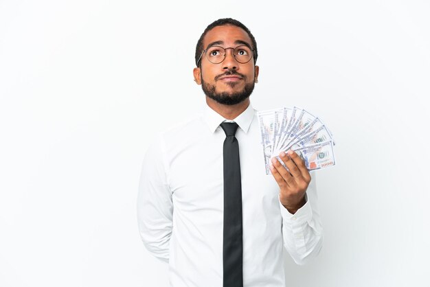 Young business latin man taking a lot of money isolated on white background and looking up