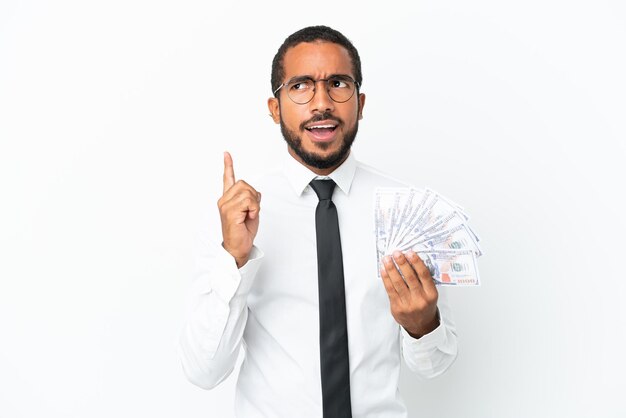 Young business latin man taking a lot of money isolated on white background thinking an idea pointing the finger up