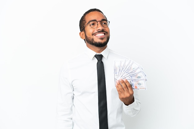 Young business latin man taking a lot of money isolated on white background thinking an idea while looking up