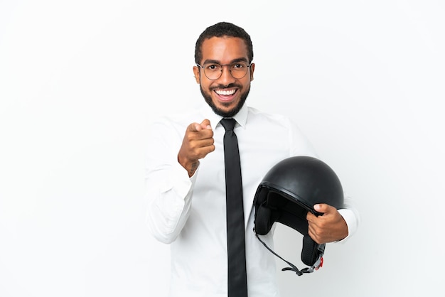 白い背景に分離されたオートバイのヘルメットを持つ若いビジネスラテン男は驚いて正面を指しています