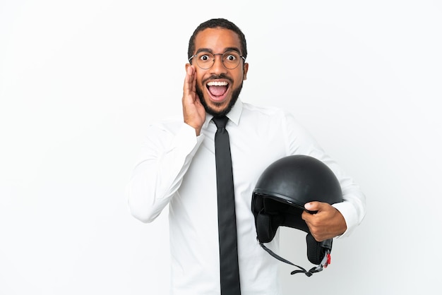 驚きとショックを受けた顔の表情で白い背景に分離されたオートバイのヘルメットを持つ若いビジネスラテン男