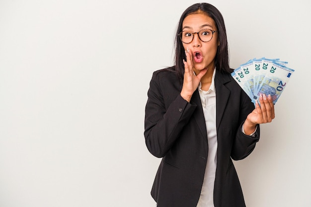 Young business latin woman holding bills coffee isolated on white background  is saying a secret hot braking news and looking aside