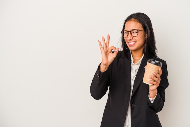 Young business latin woman holding a take away coffee isolated on white background  cheerful and confident showing ok gesture.